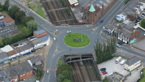 An aerial view of the bridge-roundabout on Greek Street in Stockport, with railway tracks seen underneath and homes and roads either side.