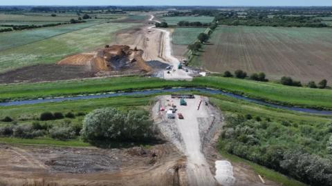 An aerial shot of two new roads on either side of the River Witham. Fields surround the roads and river. 