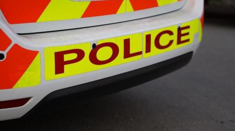 An image of the rear of a police car with the sign POLICE in red lettering on an illuminous yellow background.