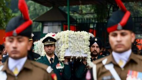 Soldiers in uniform stand guard as two officials carry a coffin decorated with flowers 