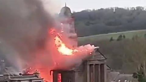 Flames coming through the roof of a church, with countryside in the distance.