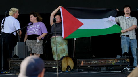 Four members of the Mary Wallopers on stage, with two on the right of the picture holding a Palestinian flag.