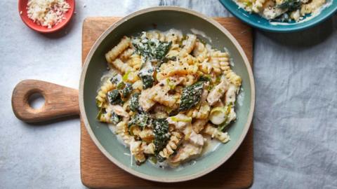 Green bowl on a brown chopping board filled with pasta and spinach, topped with parmesan cheese