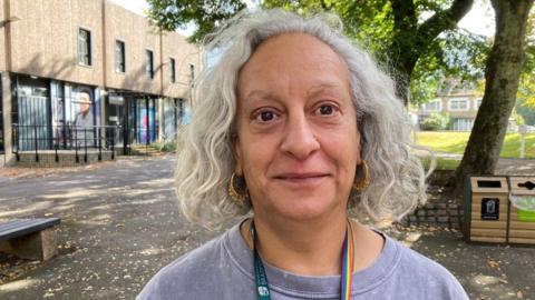 A grey-haired woman wearing a grey top with a multi-coloured lanyard.