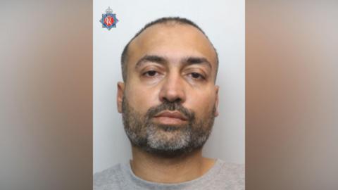 The mugshot of a man with a greying beard and close-cropped hair.