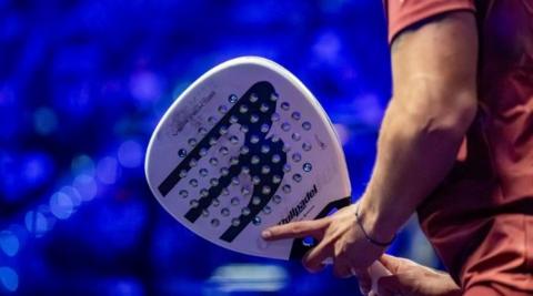 A man holding a white padel racquet with a blue background.