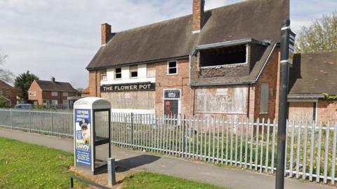 Google Street View image of the former Flower Pot pub on the Bilton Grange estate. The two-storey building is boarded up behind metal railings with its name still above one of the windows