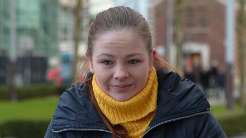 Jolene Bunting. She has brown hair tied back, wearing a yellow roll-neck jumper and navy raincoat.