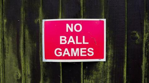 A red 'no ball games' sign on a fence