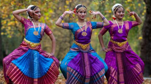 three dancers in bright, matching dresses pose for a photograph in a autumnal park