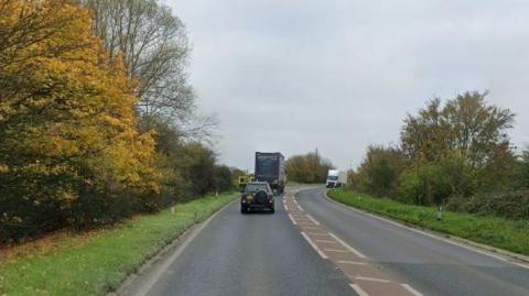 Two single carriageways of the A47 on a bend, with a lorry and a car travelling in one direction and a white lorry travelling in the other.