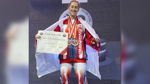 A girl wearing a red and blue tracksuit, draped in an England flag, holding a certificate