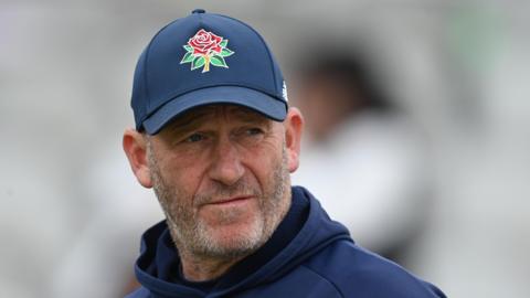 Craig White watching on, wearing a navy cap with a Lancashire red rose on it