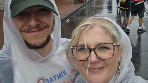 A man and a woman standing in front of the Cinderella Castle at Disney World. They are wearing clear rain ponchos