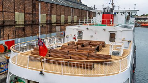 The top deck of a ferry fitted with brown wooden benches. 