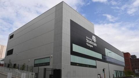 A large modern grey building, with University of Strathclyde written in large letters on the side of the building, against black panels.