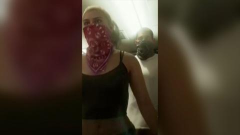 Still of GTA, a woman waring a red scarf over her mouth and a man behind her wearing a black scarf over his