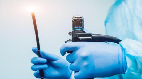 Endoscopy equipment being held by a medical professional - you can see their gloved hands and scrubs with items held in each hand