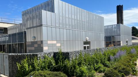 A large grey building with a chimney at the back. 