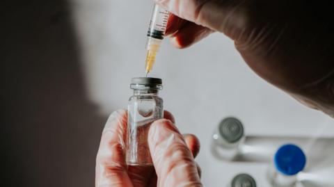 A scientist draws liquid medicine through a syringe from a vial