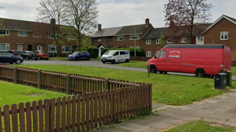 A street view of Big Meadow Road. There are several vans parked on pavements around the cul-de-sac.