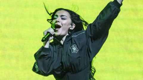  Charli XCX singing in a black outfit against a bright green background