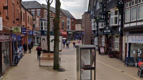 A view of Low Street which shows a pedestrianised high street. There is a phone box in the centre and a range of shops along with a pub