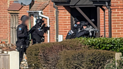 Four armed police officers at the a doorway of a property.