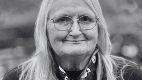 Black and white head and shoulders of Jennifer Turner in her scour uniform, with long fair hair and wire framed glasses