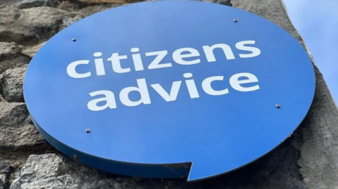 A blue Citizens Advice sign is on a stone wall