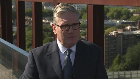 Prime Minister Sir Keir Starmer stands on a bridge overlooking a canal and railway lines.