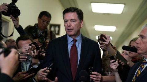 James Comey is surrounded by reporters holding phones and mics and cameras as he appears in Congress to testify in 2018. 