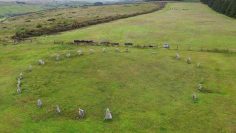 Goodaver Stone Circle on Bodmin Moor - a set of granite stones in a green field, surrounded by fencing