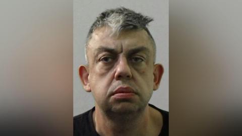 Mugshot of Monteith. He has faint stubble, short dark and grey hair and a downcast face.