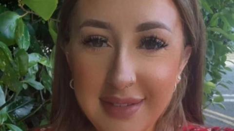 Sarah Montgomery. She has long brown hair and brown eyes, wearing a gold and earrings necklace and red floral top.
