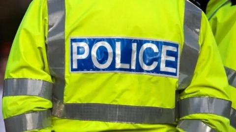 A close-up of the back of a police officer's high-vis yellow jacket, with the writing POLICE stitched into the back, on a blue background.
