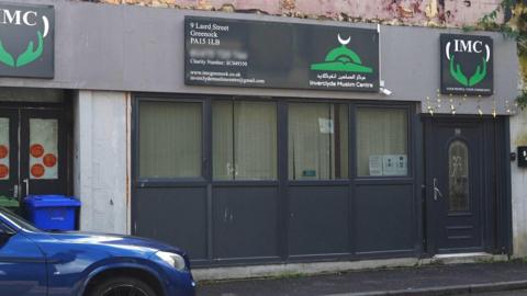 The street entrance to the mosque which has four windows and a door, with three signs saying IMC above them