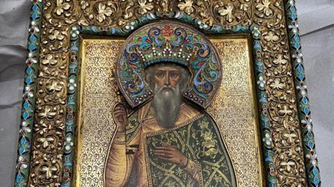 A piece of artwork with brightly coloured features. It depicts a mana with a beard wearing wearing what appears to be religious or regal clothing. The artwork is sat on light-coloured paper which seems to be the packaging it was kept in.
