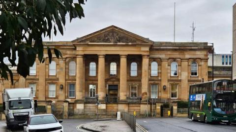 The exterior of a sandstone court building with four pillars outside the main entrance
