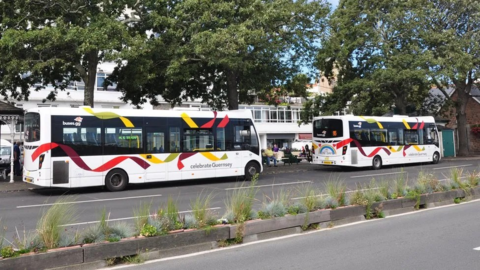 Two white buses with red and yellow livery next to a bus terminus