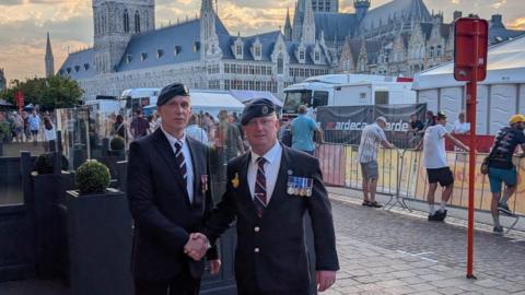 Two men in military uniforms shaking hands. In the background there is a large gothic church.