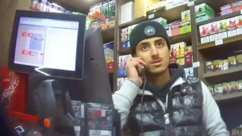 A man on his phone behind the counter of a corner shop