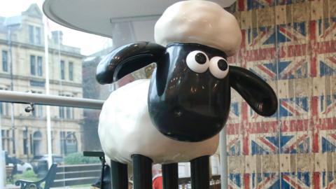 The original black and white Shaun the Sheep animation has been created into a sculpture. It has been positioned on a platform in front of a large glass window and a wall featuring Union Jack flag wallpaper.