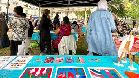 Artwork on a table at a stall with people in the background