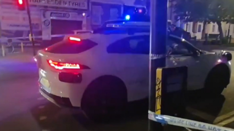 Car driving into police cordon with shops in the background