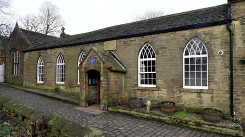 A 19th Century schoolroom - a single storey brick building on a cobbled street with a blue plaque above the door