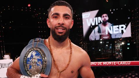A boxer with a title belt. The grey belt has a blue badge on it.