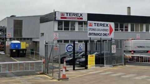 A grey building that has Terex logo across it, there are multiple cars parked there