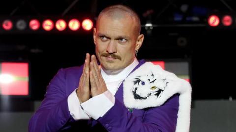 Oleksandr Usyk makes prayer hands dressed in a purple suit