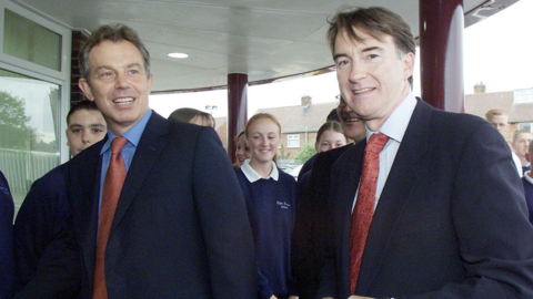Tony Blair, in navy blue suit and red tie, stands alongside Peter Mandelson, in similar attire, out on a campaign event in 2001. There are some school children behind them as they walk into a school in Mandelson's Hartlepool constituency, which he left the same year. 